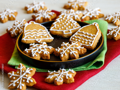 Homemade gingerbread cookie in shape of snowflakes and bells decorated with icing on black plate on green and red napkins. Traditional Christmas food. Christmas and New Year holiday concept.