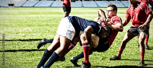 Digital composite image of team of rugby players tackling each other to win the ball in stadium