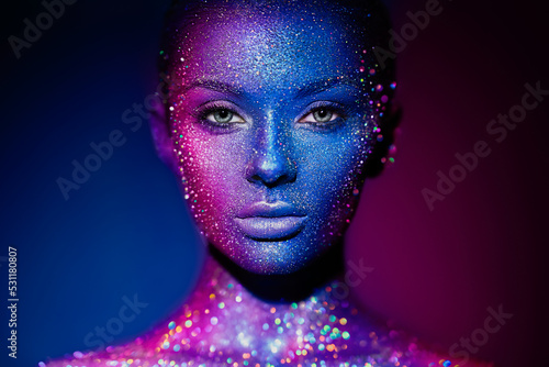 Fashion model woman in blue bright sparkles and neon lights posing in studio. Portrait of beautiful young woman. Art design colorful glitter glowing make up