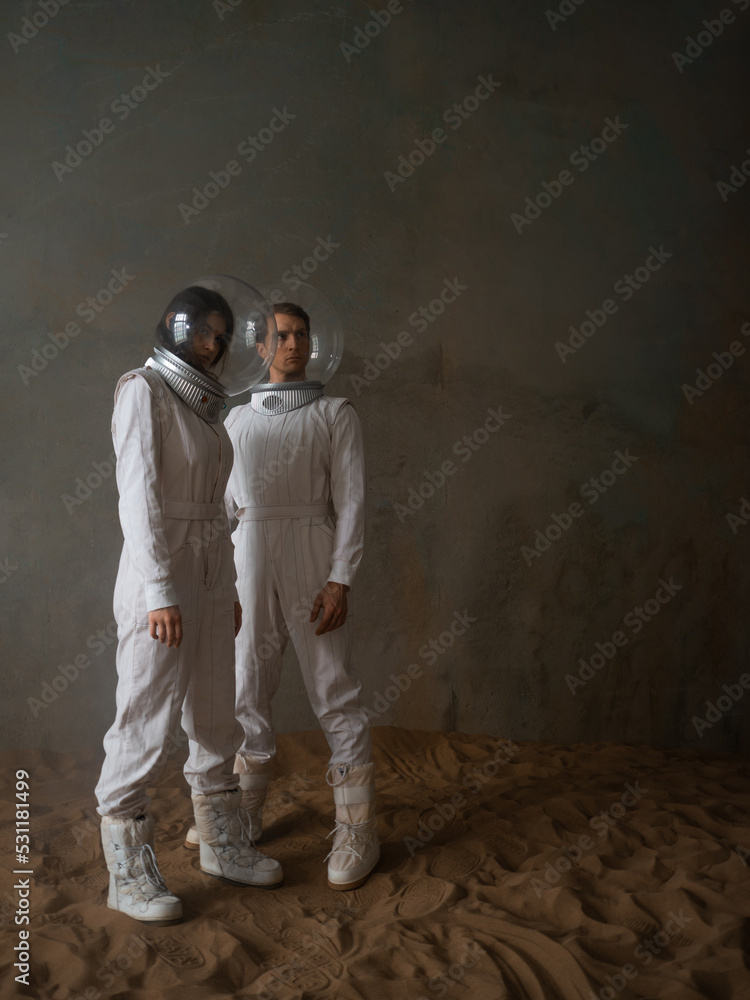 a man and a woman in white futuristic spacesuits explore the planet, astronauts in an empty colony on the sand,