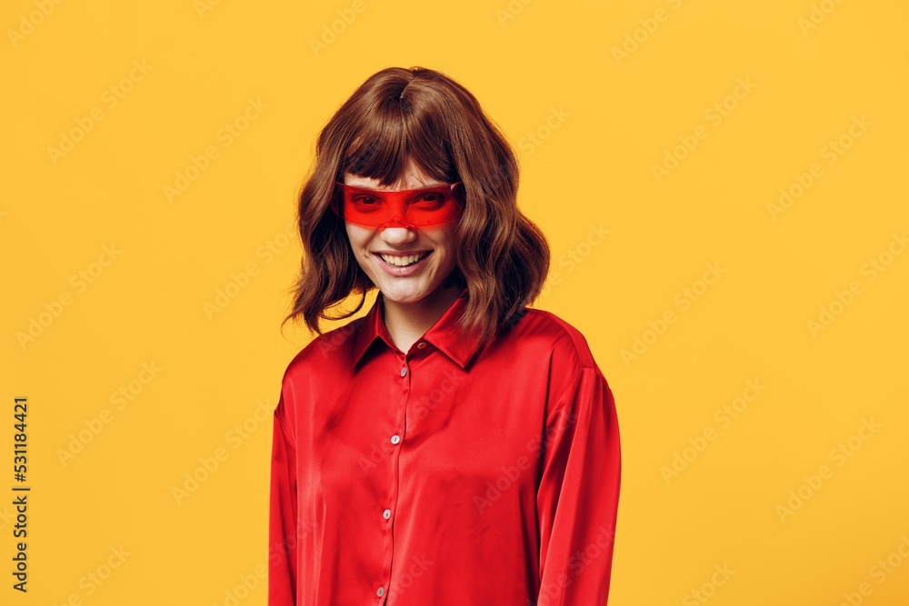 a stylish woman stands on a yellow background in a red shirt and glasses of an interesting shape smiling pleasantly at the camera a stylish woman stands on a yellow background in a red shirt and glasses of an interesting shape smiling pleasantly at the camera