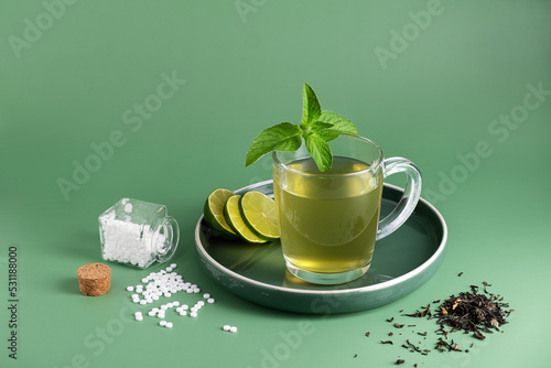 A cup of green tea with mint leaves and lime slices on a green background. There are stevia sweetener tablets in a glass jar. The concept of healthy eating. Copy space, horizontal orientation photo