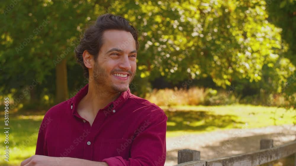 Portrait of casually dressed smiling mature man leaning on wooden fence on walk in summer countryside - shot in slow motion Portrait of casually dressed smiling mature man leaning on wooden fence on walk in summer countryside - shot in slow motion