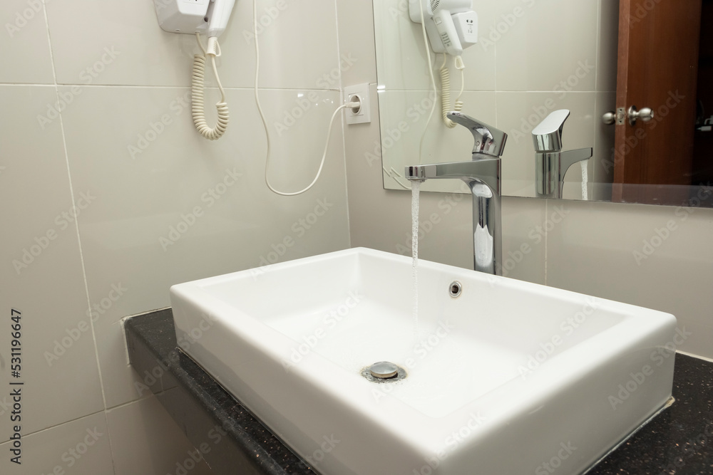 Bathroom sink basin and closed chrome faucet washbasin. Silver taps on ceramic beige tiles wall, square white wash basin. Modern minimal concept. Bathroom sink basin and closed chrome faucet washbasin. Silver taps on ceramic beige tiles wall, square white wash basin. Modern minimal concept.