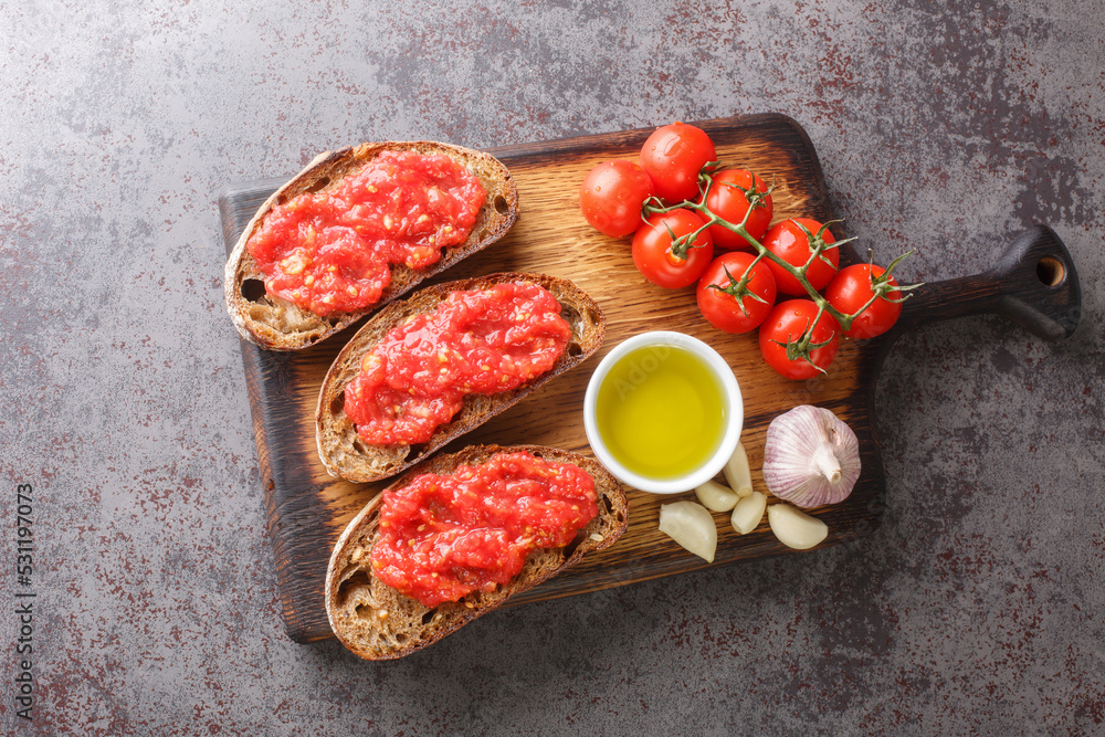 Spanish tomato toast pan tomaca or tostadas con tomate closeup on the wooden board on the table. Horizontal top view from above Spanish tomato toast pan tomaca or tostadas con tomate closeup on the wooden board on the table. Horizontal top view from above