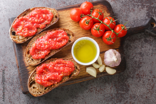 Catalan Pan con Tomate Spanish toasted bread rubbed with fresh garlic and ripe tomato, then drizzled with olive oil closeup on the wooden board on the table. Horizontal top view from above photo