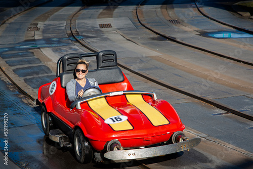 Happy woman driving a miniature car at an amusement park ride during a fun family vacation. Driving a toy car is a lot of fun. photo