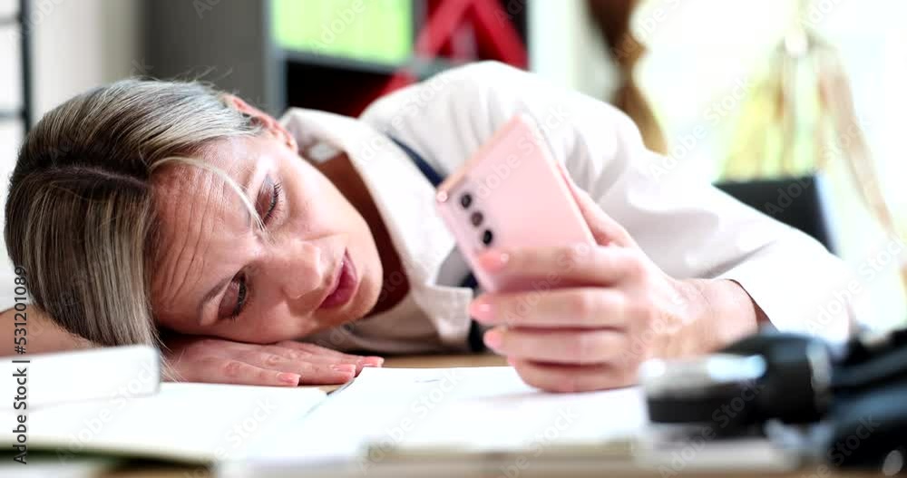 Tired female doctor lies on table and looks into phone Tired female doctor lies on table and looks into phone