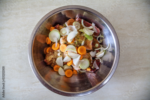 A metal bowl with raw sliced meat, pickled with spices, and vegetables for further cooking.