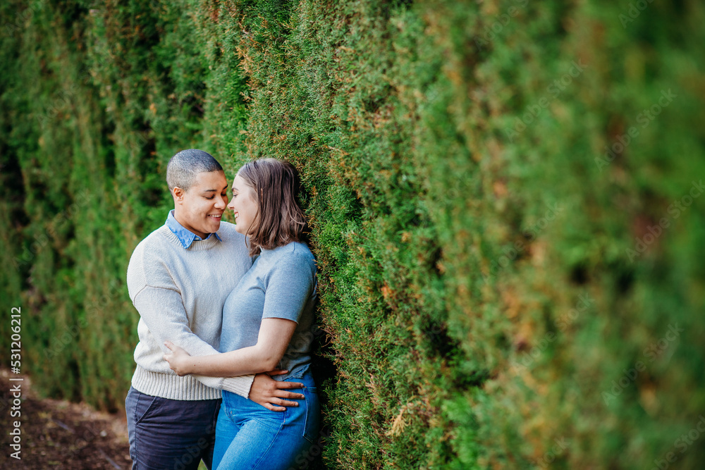 lgbtqi couple hugging each other and looking at each others faces while leaning on a wall with moss lgbtqi couple hugging each other and looking at each others faces while leaning on a wall with moss