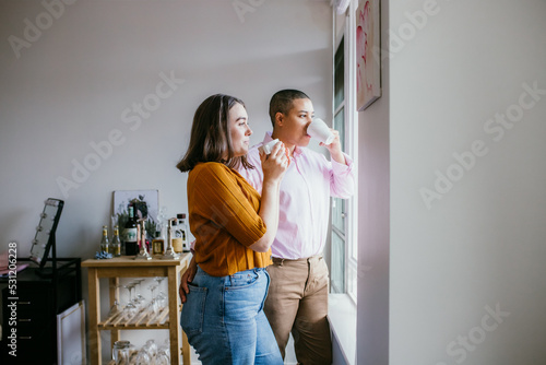 smiling lgbtqi couple drinking coffee looking outside the window photo