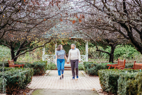 smiling lgbt  couple holding hands with dead trees, shrubs and wooden benches on the side photo