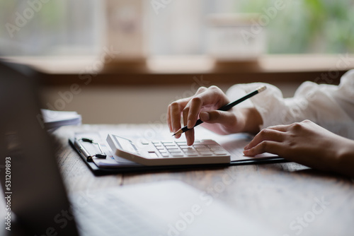 Close up of businesswoman or accountant hand holding pen working on calculator to calculate business data, accountancy document and laptop computer at office, business concept. photo