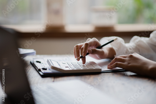 Photos Close up of businesswoman or accountant hand holding pen working on calculator to calculate business data, accountancy document and laptop computer at office, business concept