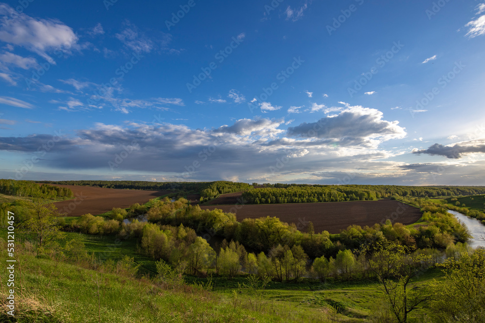 View from the hill to plowed farmland. Landscape with a river, arable land and green trees.