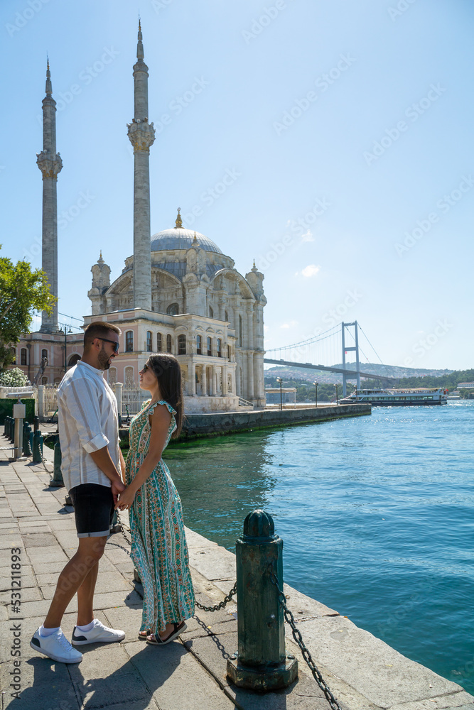 Fototapeta premium Couple in love gazing into each other's eyes with the ortakoy mosque and the famous istanbul bridge in the background.