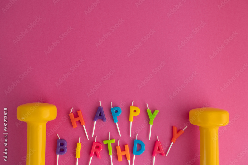 Two yellow heavy dumbbells with colorful Happy Birthday cake candles