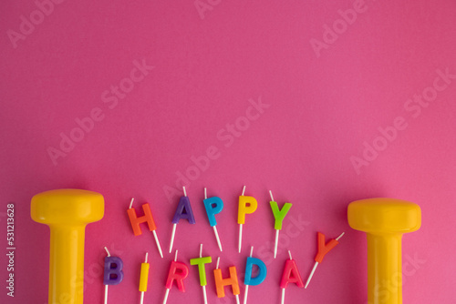 Photography Two yellow heavy dumbbells with colorful Happy Birthday cake candles letters