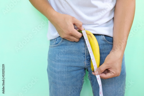 Size matters concept and penis size measurement.  Young Asian man measuring a banana using tape measure on his crotch. photo