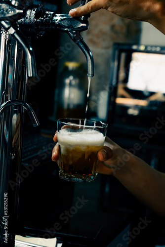 Hand serving beer in glass using tap. Bartender pouring beer while standing at bar counter.  Barman hand at beer tap pouring an draught beer. photo