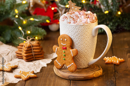 a mug of hot chocolate with marshmallows stands on a wooden background among Christmas decorations and ginger man cookies. Christmas warming drink, cocoa with cinnamon and marshmallow. new year