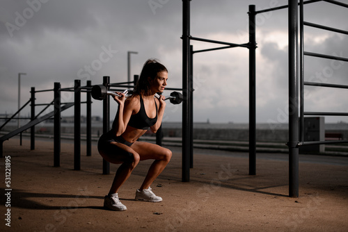 healthy woman standing on bent knees and holding barbell on her shoulders.