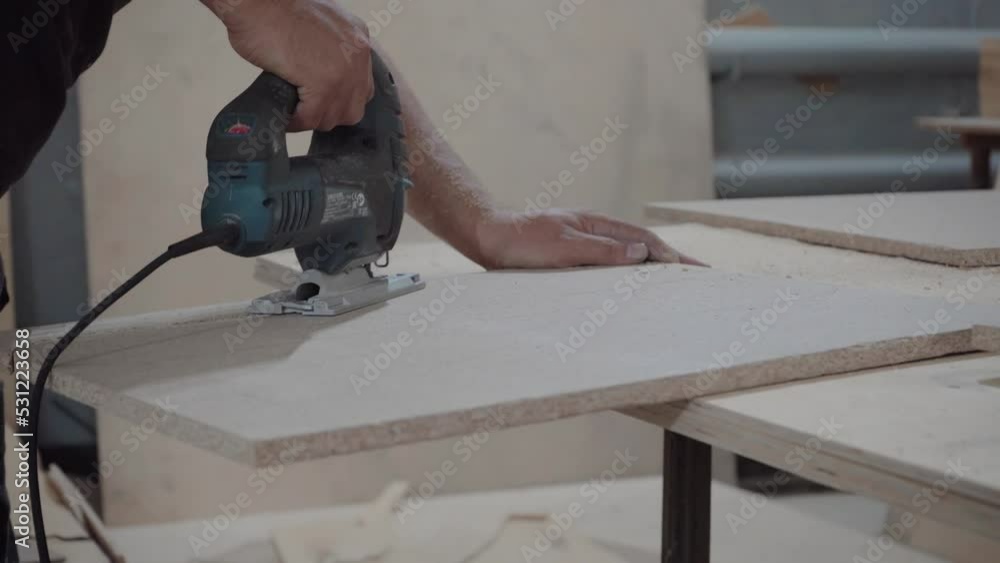 A factory worker cuts a tree with an electric jigsaw. Chipboard sawdust is flying A factory worker cuts a tree with an electric jigsaw. Chipboard sawdust is flying