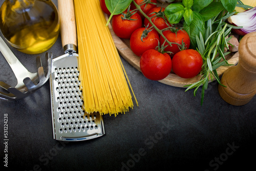 Spaghetti and ingredients for preparing pasta on a dark background, top view.