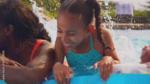 Smiling multi-generation family on summer holiday in swimming pool floating on airbed and splashing- shot in slow motion