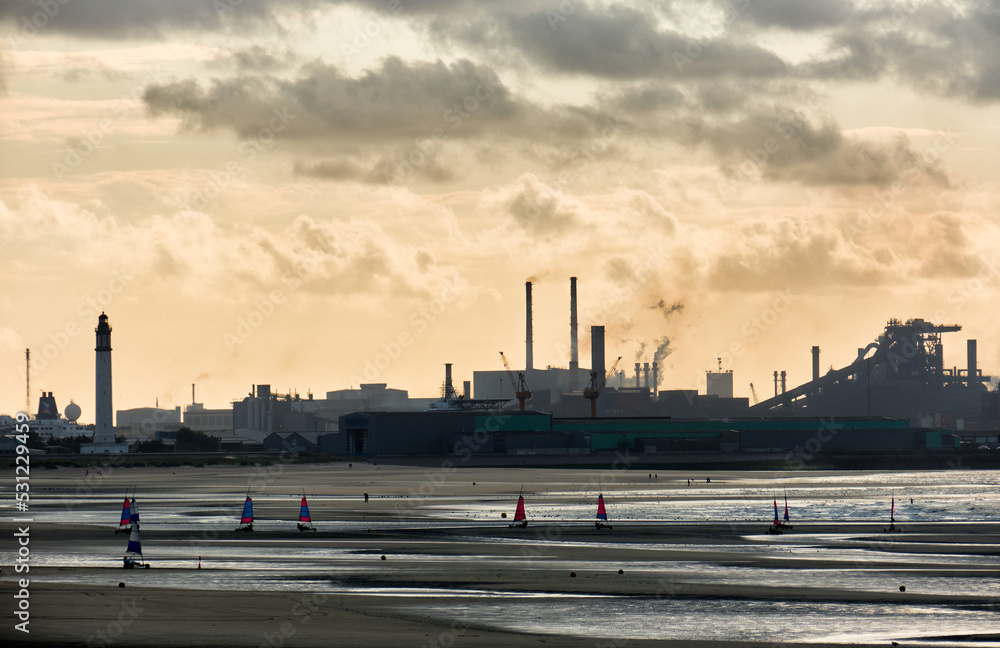 low tide and a steelworks in silhouette and port with loading cranes and containers of the port of Dunkirk, France