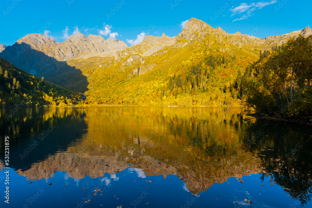 Beautiful autumn landscape. Birches with yellow foliage on the shore of a mountain lake