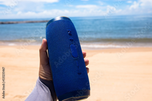 Photo of a man hand holding a portable speaker at the beach 