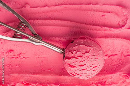 Top view of scoop of pink cold sweet ice cream or sorbet made with juicy red berries, raspberry or strawberry in metal silver serving spoon on textured gelato background. Refreshing natural dessert