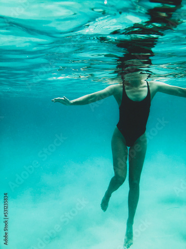 Mature woman's athletic body treading water from underwater perspective in ocean