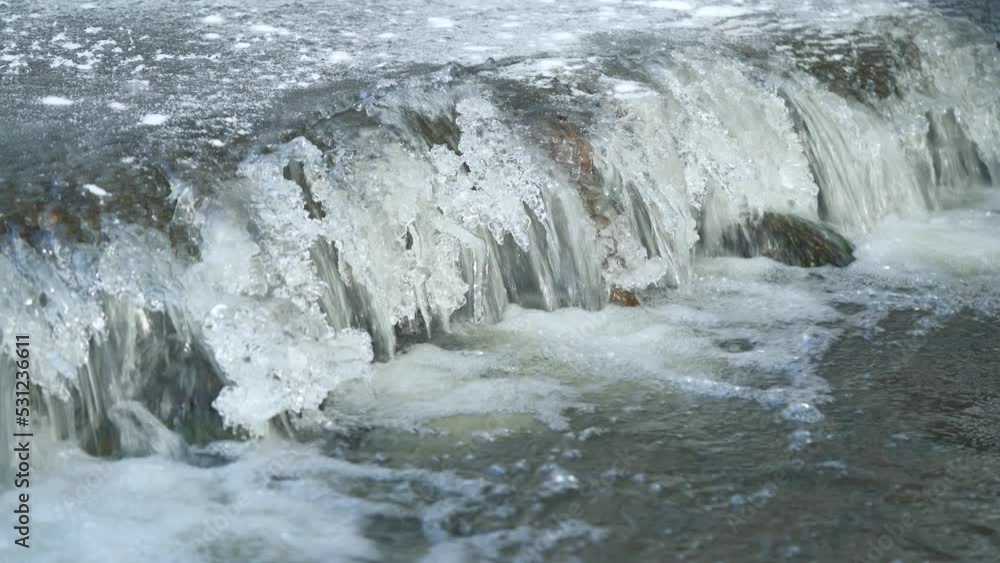 Ice on frozen river, closeup detail, water flows over small cascade - winter background Ice on frozen river, closeup detail, water flows over small cascade - winter background
