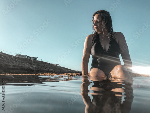 Woman in black bathing suit posing on waters edge in calm ocean photo