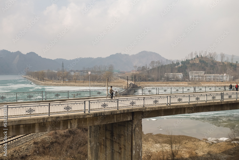 Cyclist crossing a bridge in small provincial town, Democratic Peoples's Republic of Korea (DPRK), North Korea