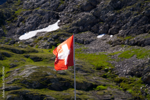 Swiss flag waving at Swiss mountain Pass Susten with Tschingelfirn glacier in the background on a sunny summer day. Photo taken July 13th, 2022, Susten Pass, Switzerland.