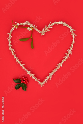 Christmas heart shape wreath symbol of love gold glitter tree decoration with holly berries and mistletoe. Traditional composition for the festive Xmas and New Year holiday season.