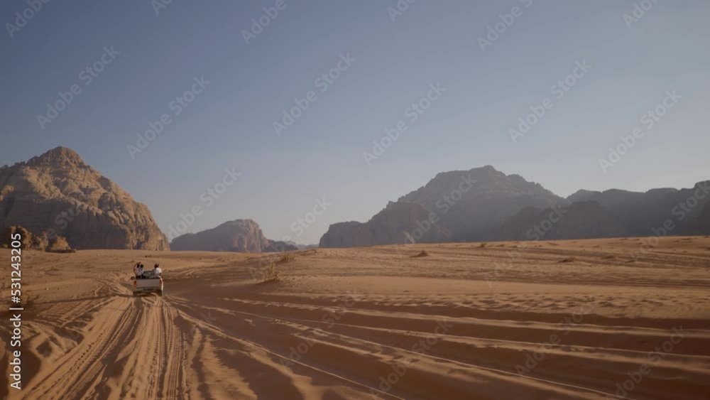 Off-road 4x4 SUV with tourists sit down on the rear body follows the tracks on the red sand of the Wadi Rum desert. Off-road 4x4 SUV with tourists sit down on the rear body follows the tracks on the red sand of the Wadi Rum desert.