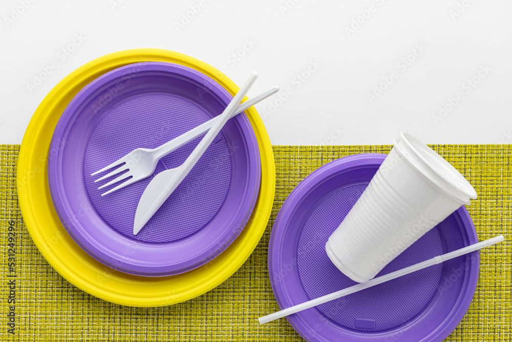 A set of multi-colored disposable tableware on a white background, a yellow plastic napkin, top view. A set of multi-colored disposable tableware on a white background, a yellow plastic napkin, top view.