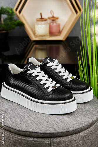Stylish black female shoes on gray pouf background in shop, copy space. New sneakers, close up. Beauty and fashion concept.