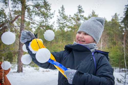 In the winter afternoon in the forest, a girl makes snowballs with a snowball and decorates tree branches.