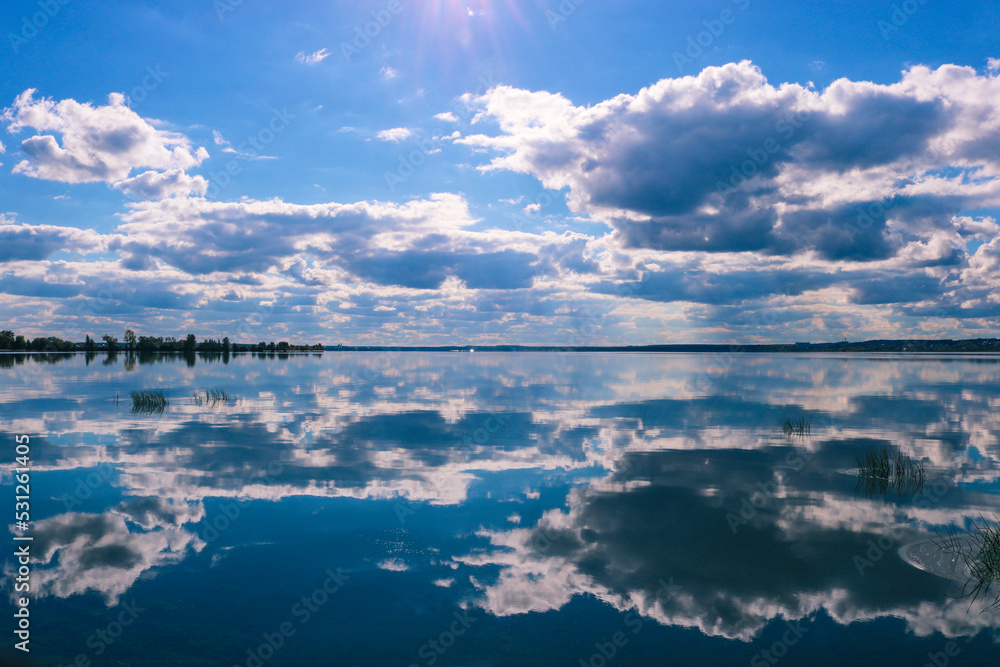Summer landscape - the sky with cumulus clouds is reflected in the water surface of the lake.