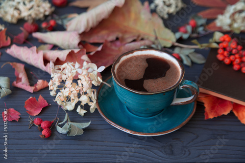 Autumn mood, a cup of coffee among autumn leaves on a wooden dark table. Texture of leaves and berries.