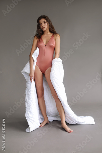 Fashion model standing in the bright studio posing wrapped in the white blanket.