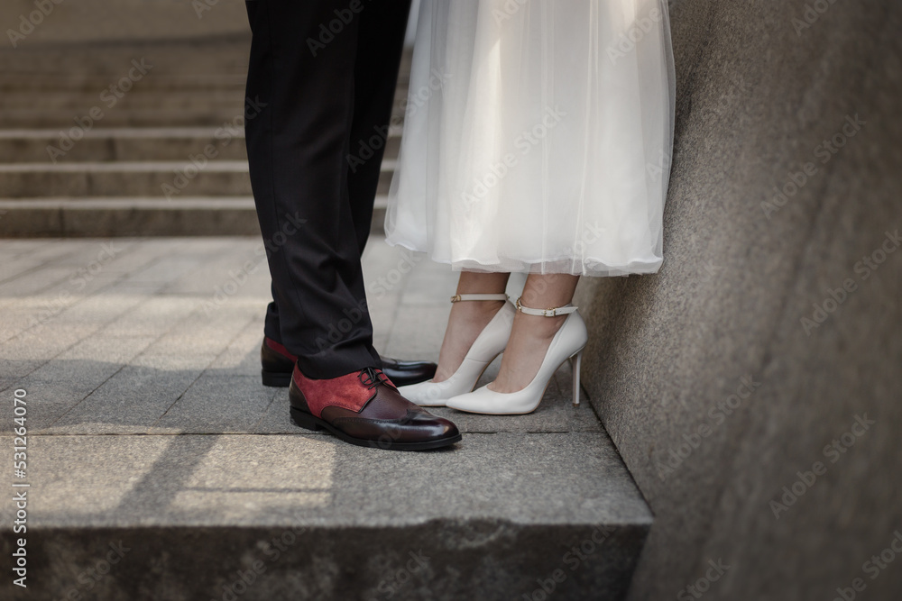 A couple of newlyweds are standing, legs in shoes close-up. Newlyweds without faces. Wedding shoes. City walk of the newlyweds.