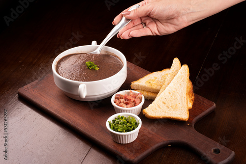 dipping spoon of bean broth and seasonings in cattail, bacon, chives, wood close-up