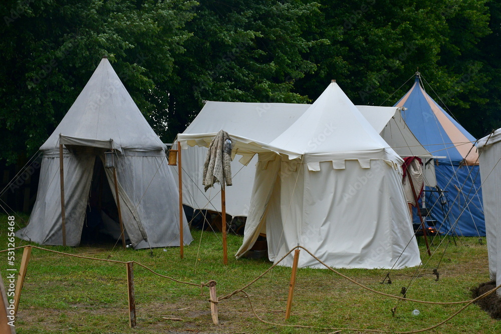 A close up on a tent made out white cloth with a wooden frame and ropes supporting it seen during a big medieval folklore festival or fair right before a massive thunderstorm and rainfall A close up on a tent made out white cloth with a wooden frame and ropes supporting it seen during a big medieval folklore festival or fair right before a massive thunderstorm and rainfall