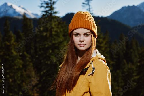 Young woman tourist portrait in yellow raincoat traveling and hiking in the mountains. Hiking in nature in the sunset